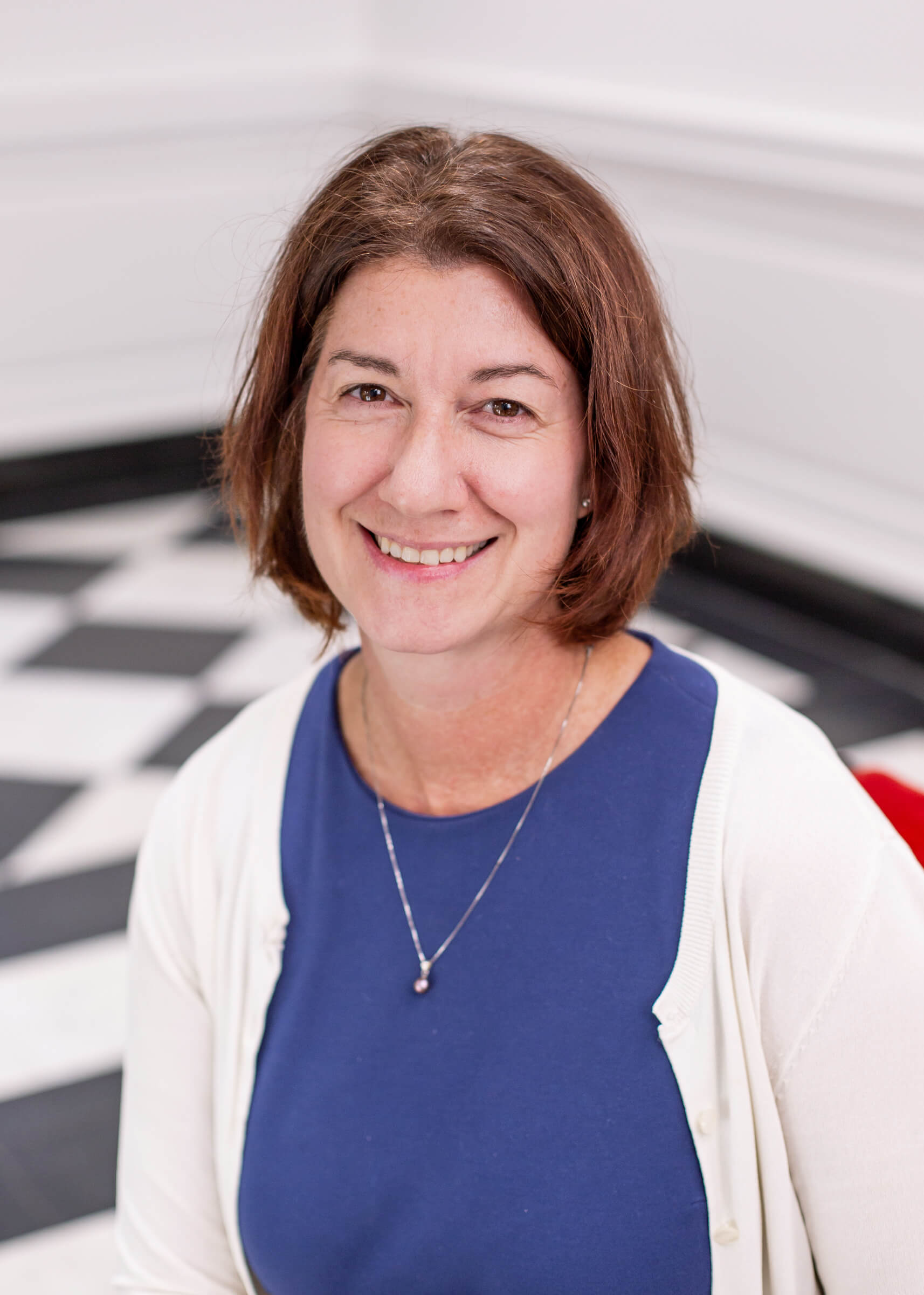 Laura Bellows sits in a red chair that is on a floor with a checkerboard pattern.