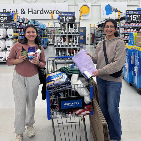 Two people stand by a shopping cart filled with items.
