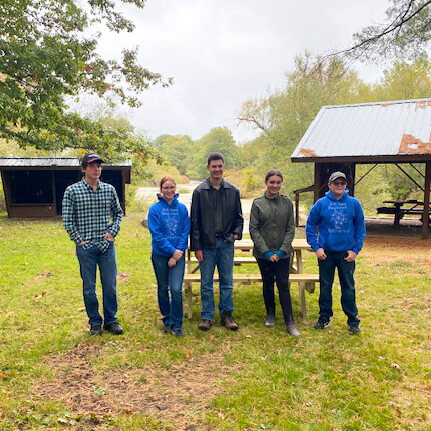 Five people stand in front of a picnic table and bench they helped build