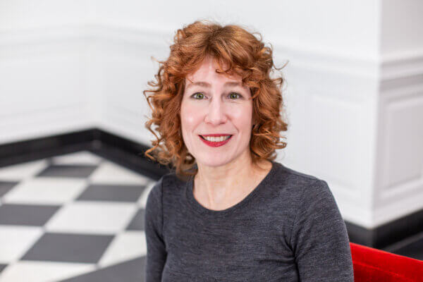 Kim Kopko sits on a red chair with a checkerboard floor behind her