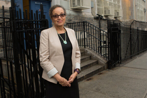 A photo of Jackie Davis-Manigaulte standing in front of a fence with a building behind her.